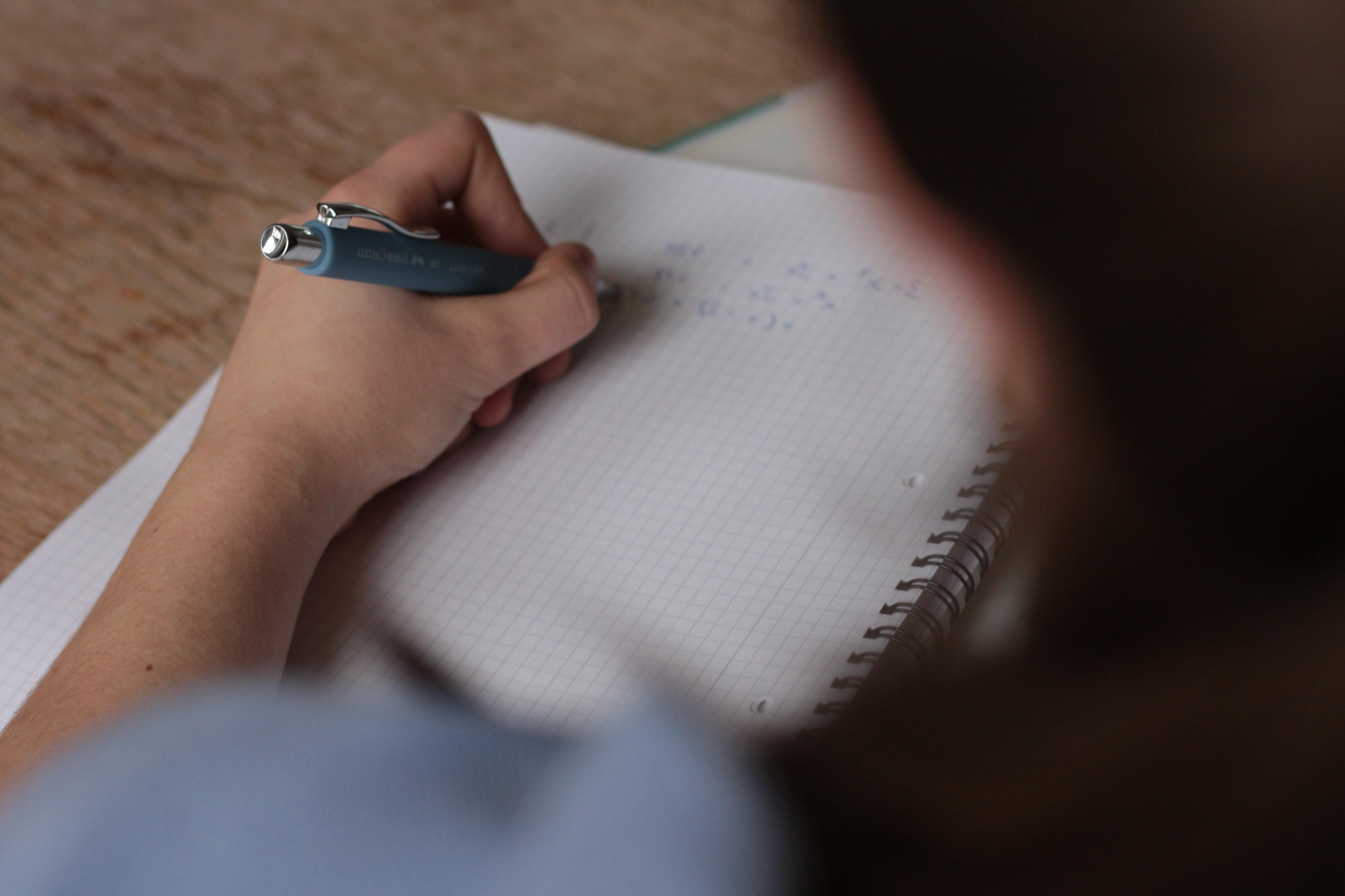 A student using a pen and graph paper to complete math problems