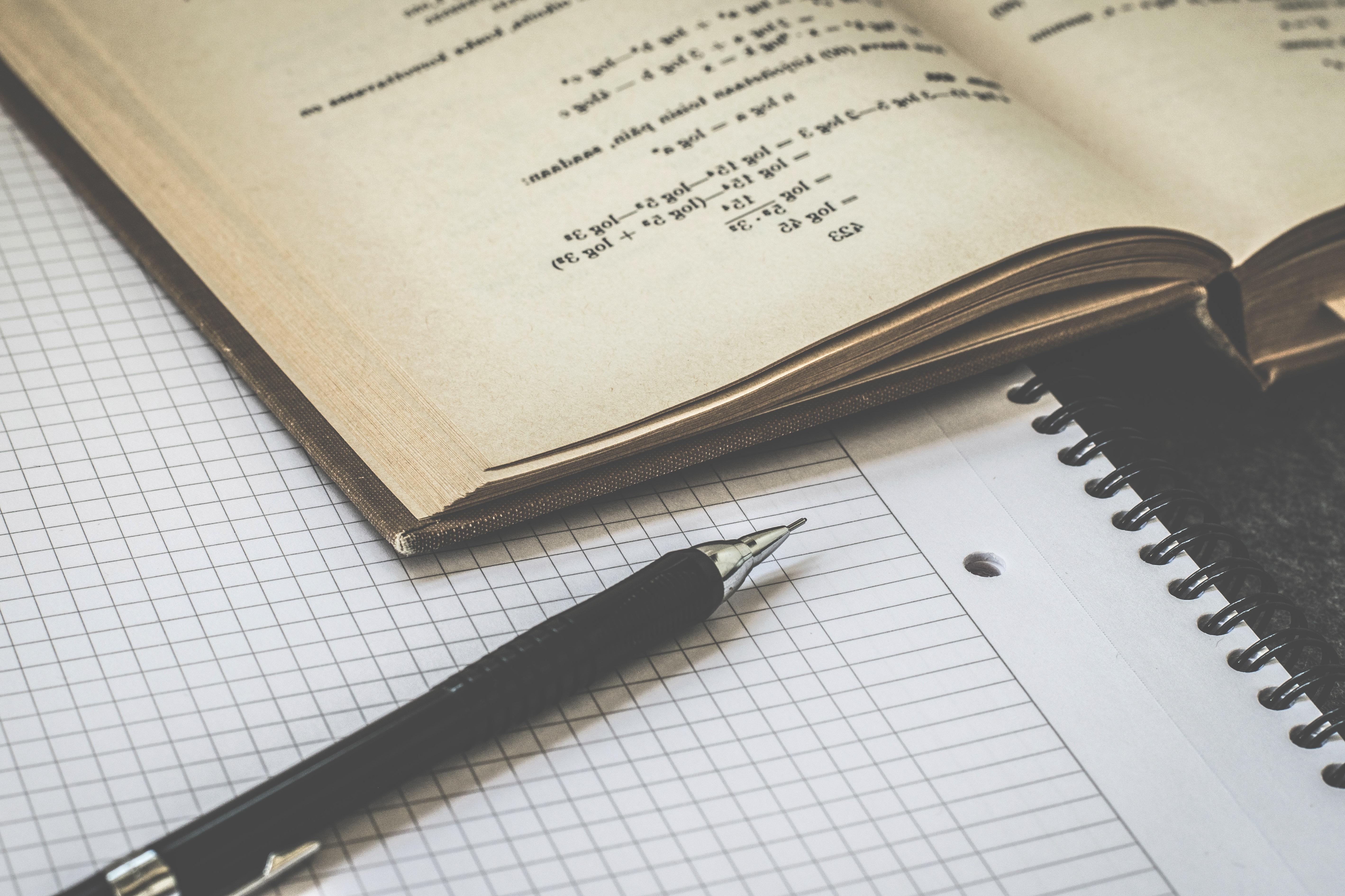 A math textbook sitting on graph paper with a pen